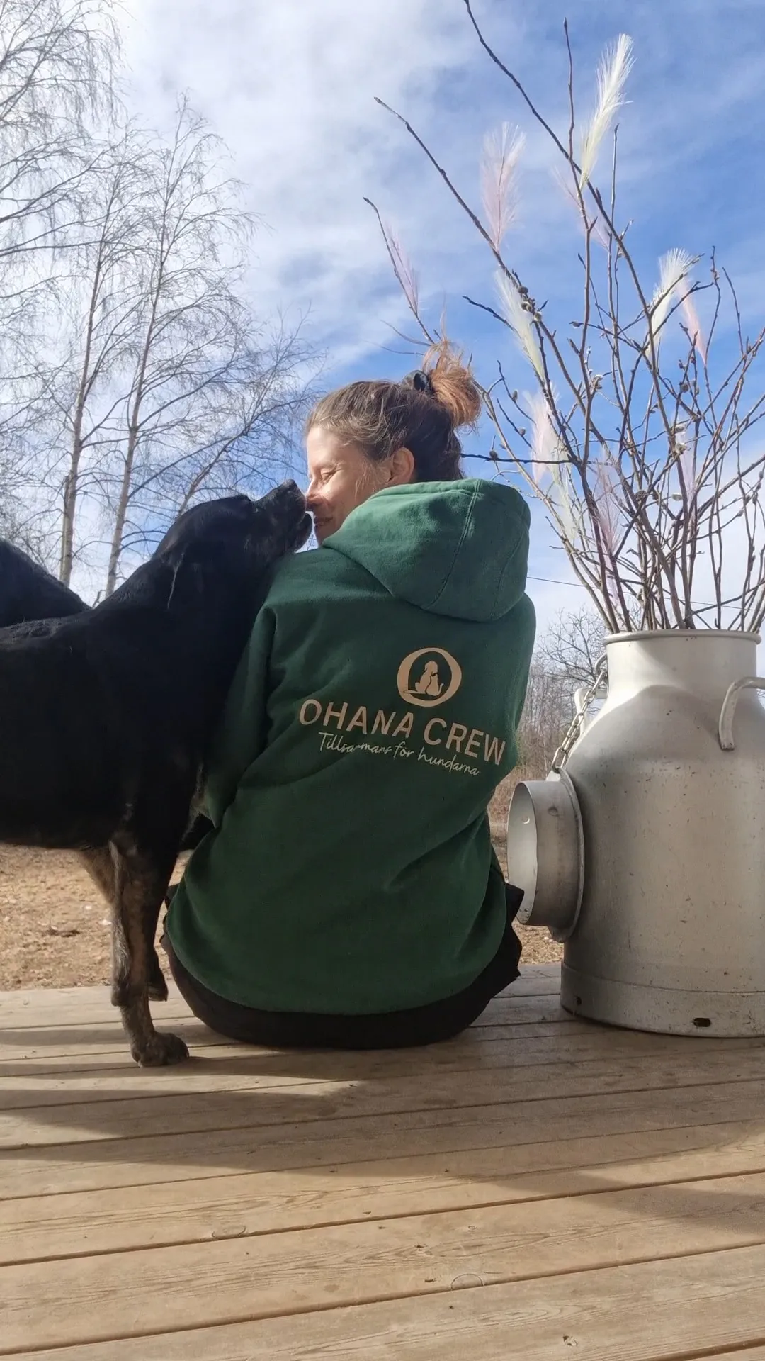 Person i grön Ohana Crew-tröja får en puss av en hund utomhus.
